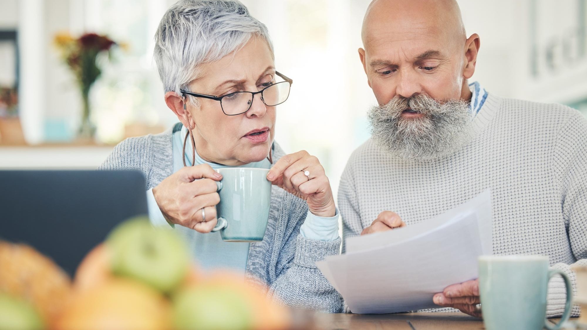 Laptop senior couple and finance documents in home for budget savings or taxes in house Computer retirement and man and woman with paperwork for financial planning insurance or bills with coffee