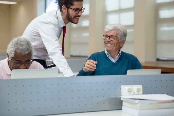 A classroom scene in Portugal where seniors learn computer skills from a young instructor. Engaged and smiling.