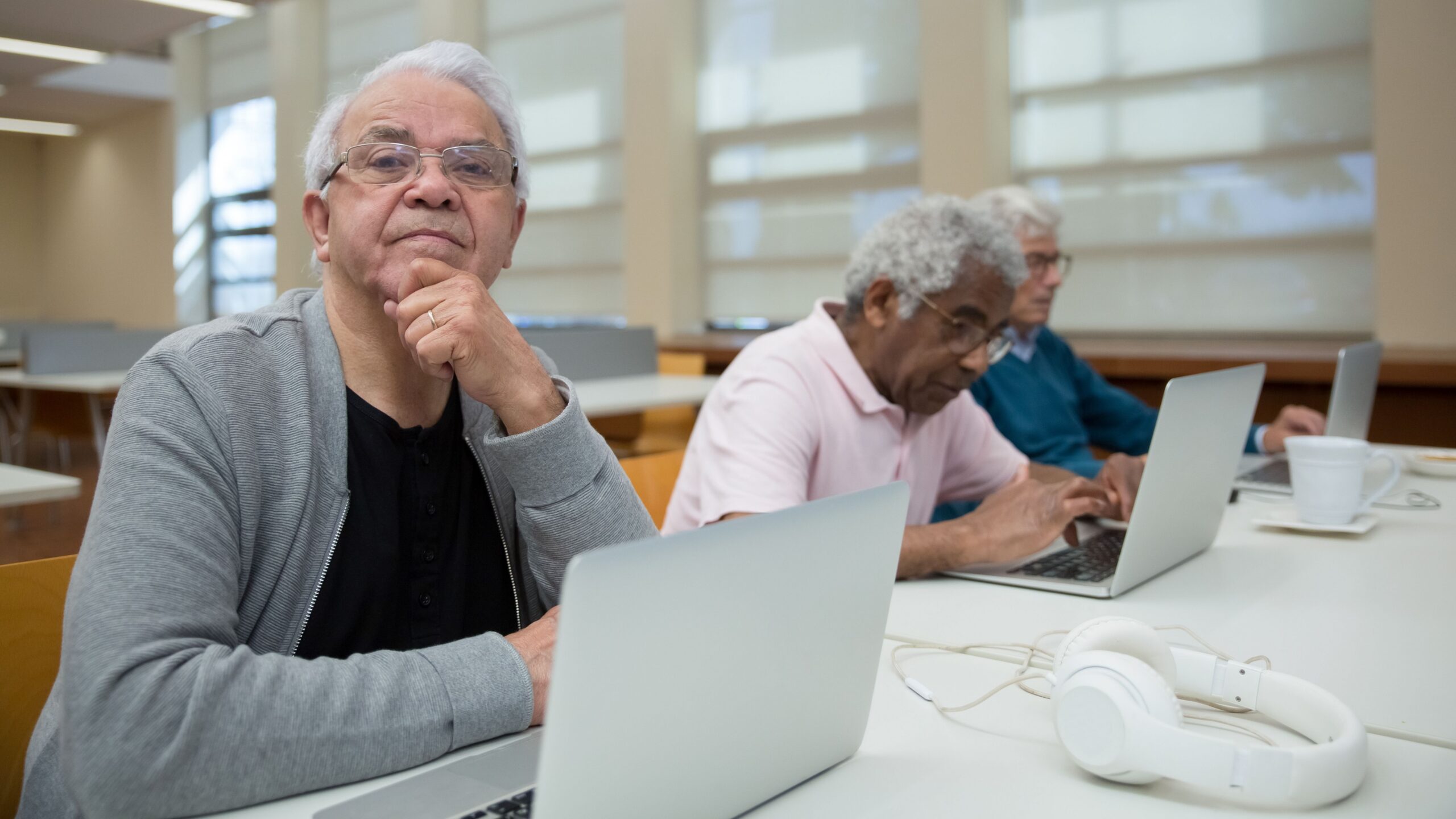 Three senior men engaged with laptops in a library environment, promoting lifelong learning.