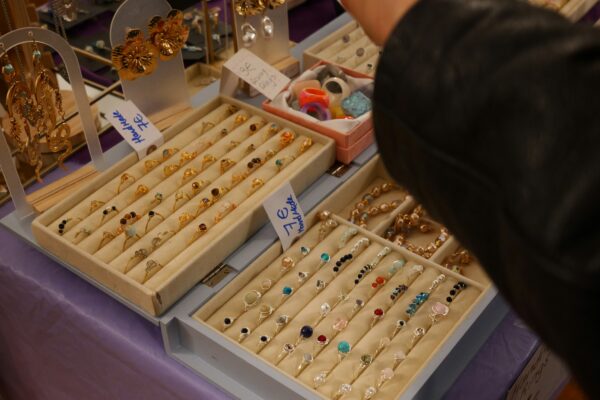 A person's hand browsing trays of rings and jewelry.