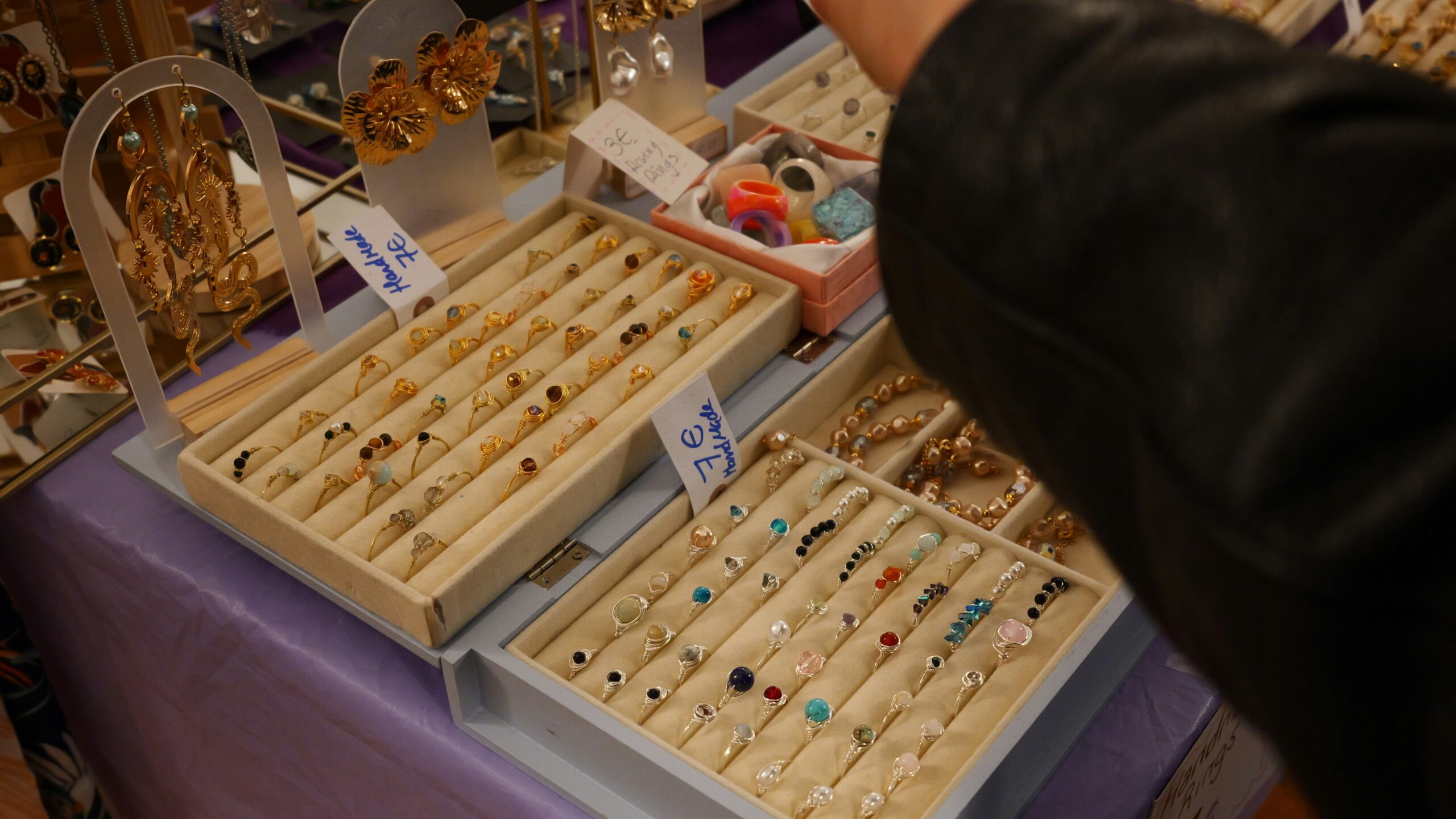 A person's hand browsing trays of rings and jewelry.
