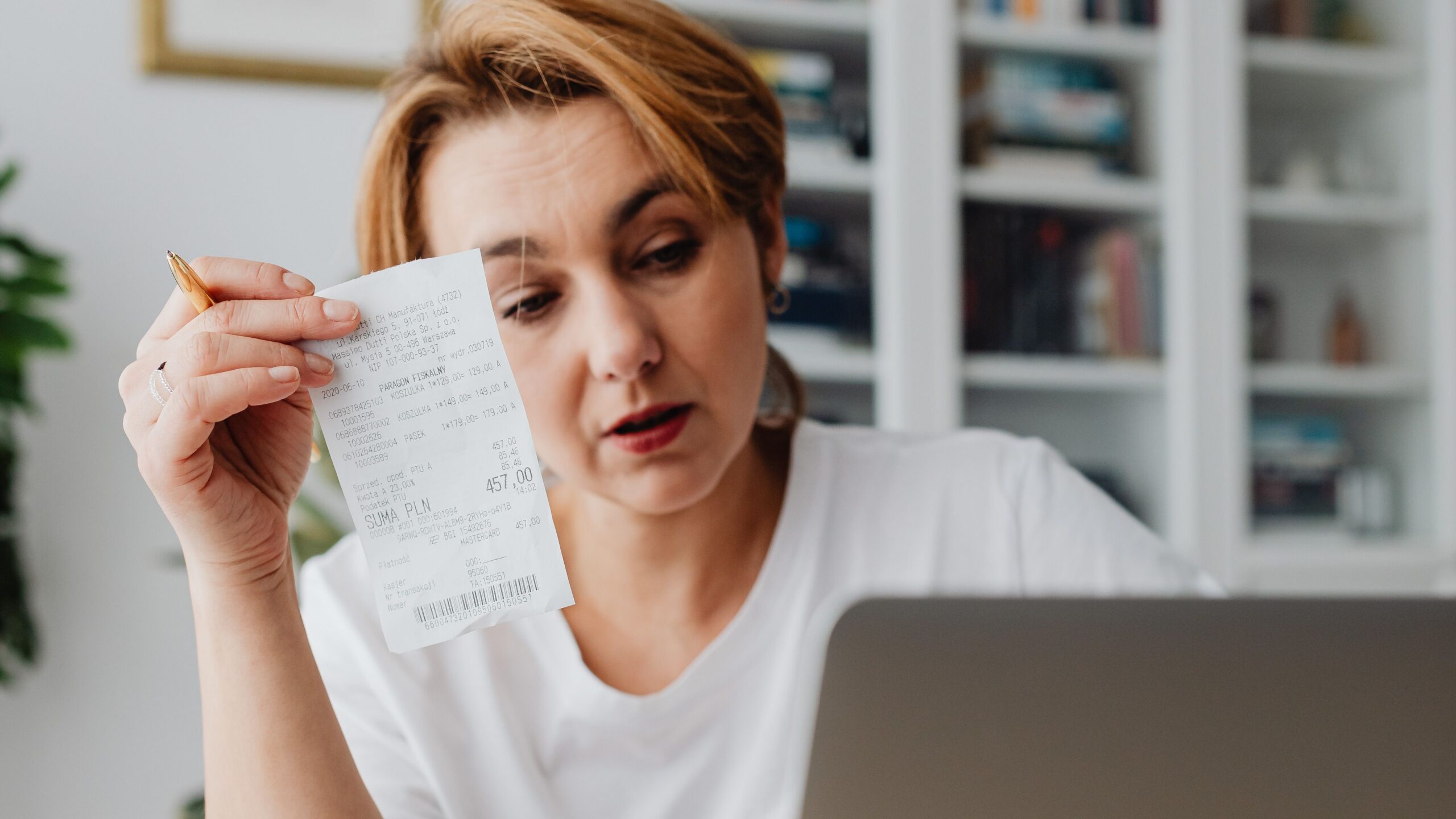 Woman using laptop while managing finances with receipts and cash on the table.