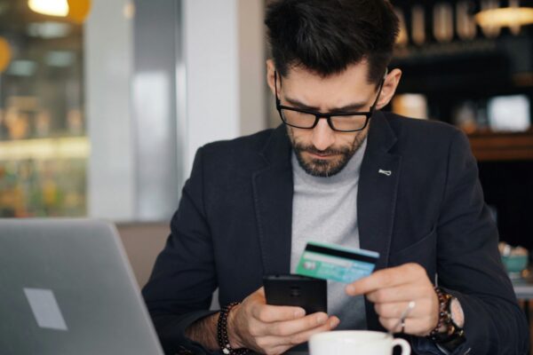 a man sitting at a table looking at his cell phone and holding a credit card