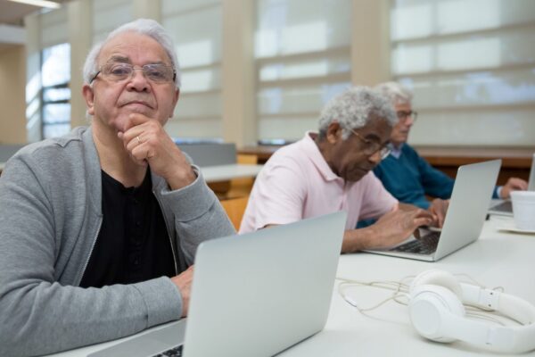 Three senior men engaged with laptops in a library environment, promoting lifelong learning.
