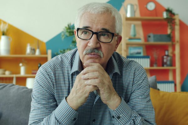 Elderly man with glasses resting chin on hands.