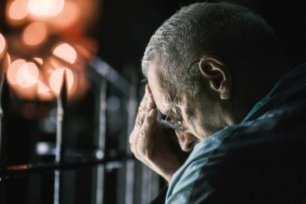 Elderly man with hand on forehead at night.