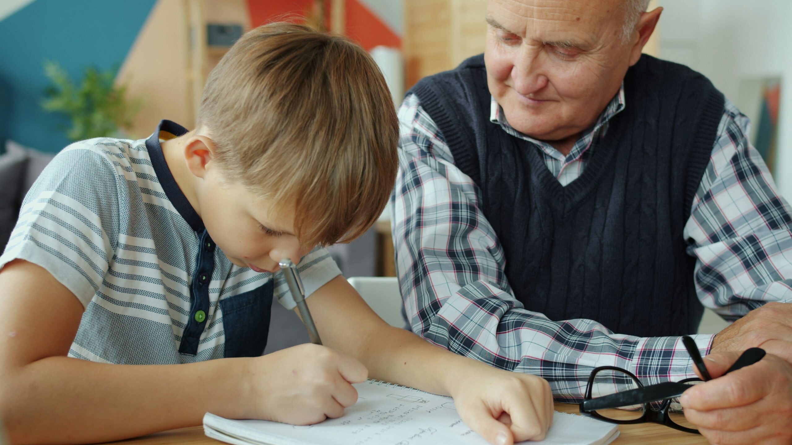 Grandfather helps grandson with homework at table.