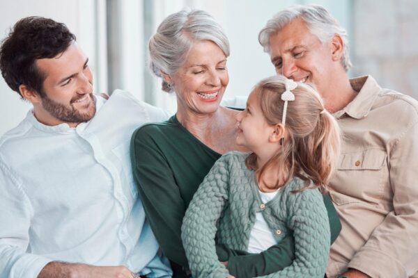 Grandparents girl and happy with dad on sofa for hug care or bonding with love in family home lounge Elderly people kid and father with smile relax and conversation on living room couch in house