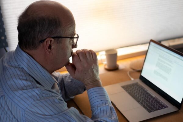 technology, oldness and lifestyle concept. Senior man in eyeglasses working with laptop computer at home and thinking on document.