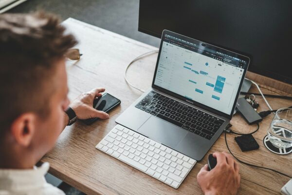 man holding mouse and iPhone while using Macbook Pro