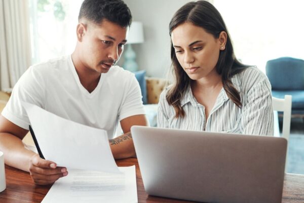 Couple conversation and paperwork with laptop in home for asset management savings fund and budget review Computer man and woman with mortgage research financial discussion and documents for tax
