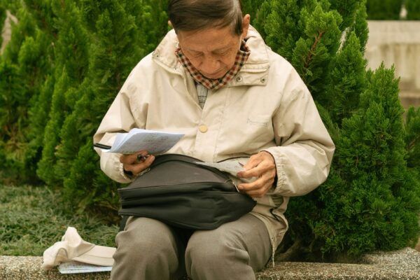 Elderly person sitting outdoors reading documents