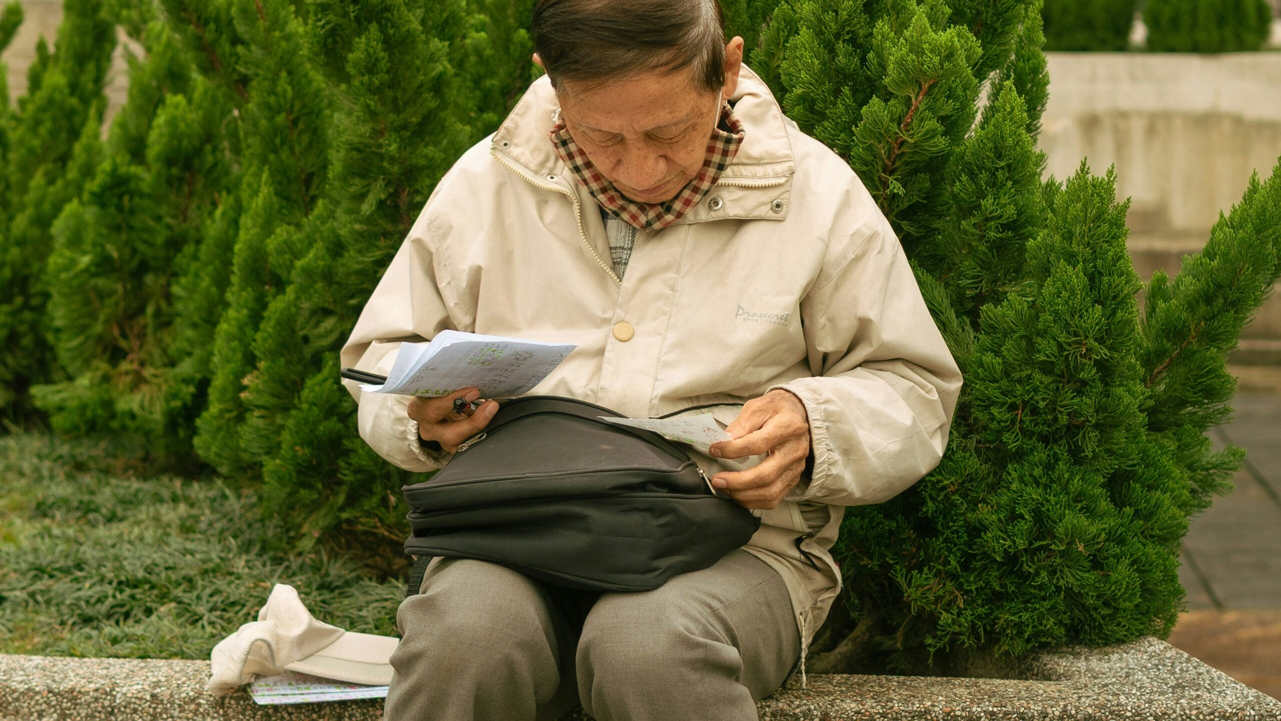 Elderly person sitting outdoors reading documents