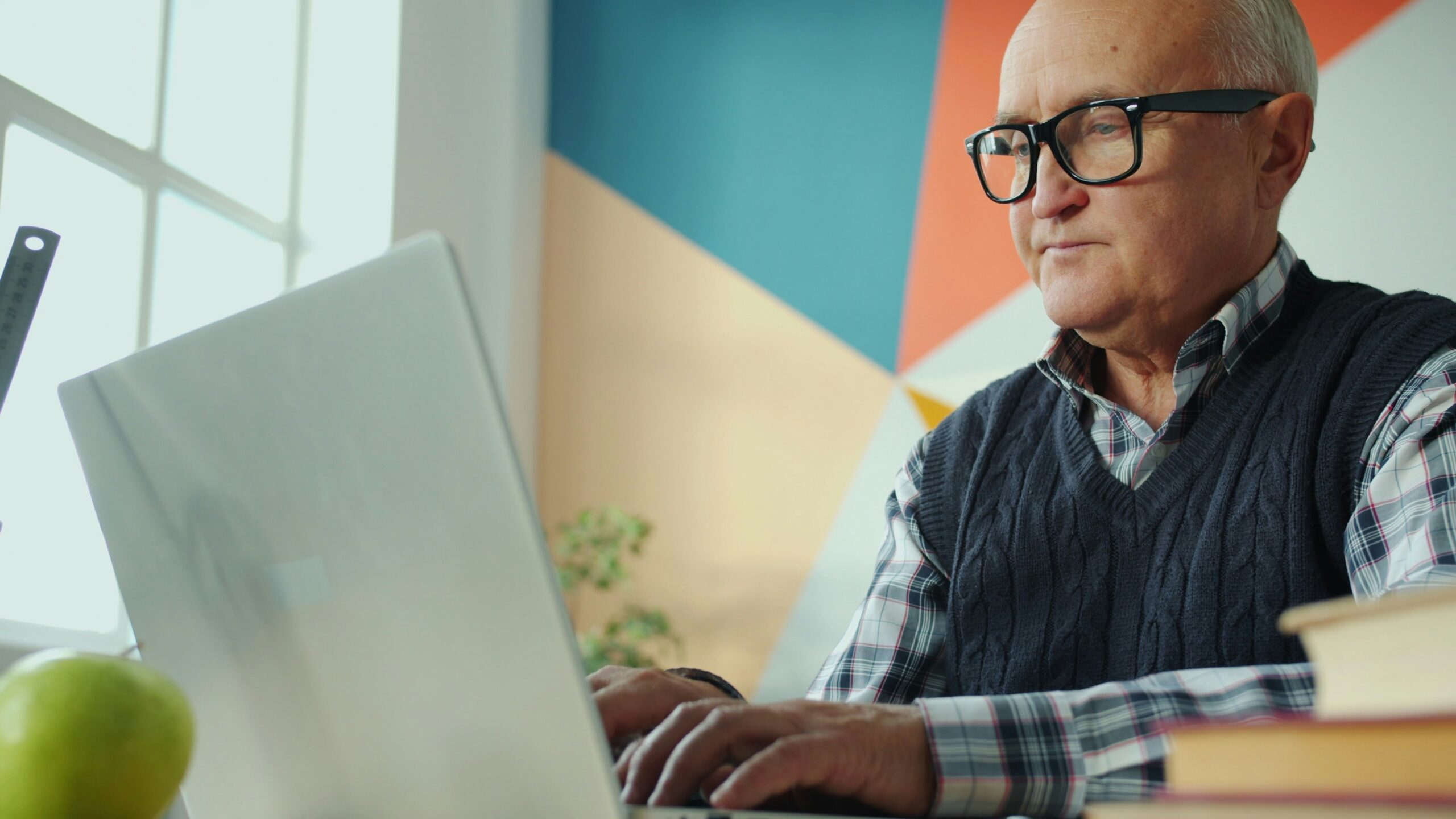 Elderly man with glasses working on a laptop.
