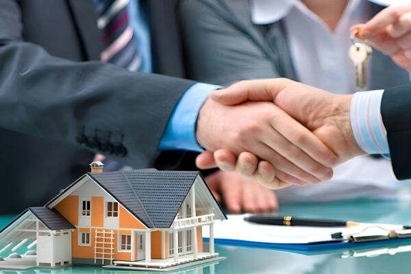 Two men shaking hands over a house model and keys.