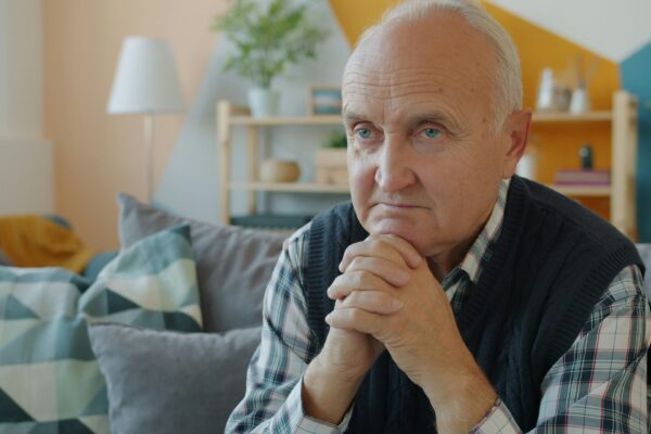 Elderly man sitting on a couch with hands clasped.