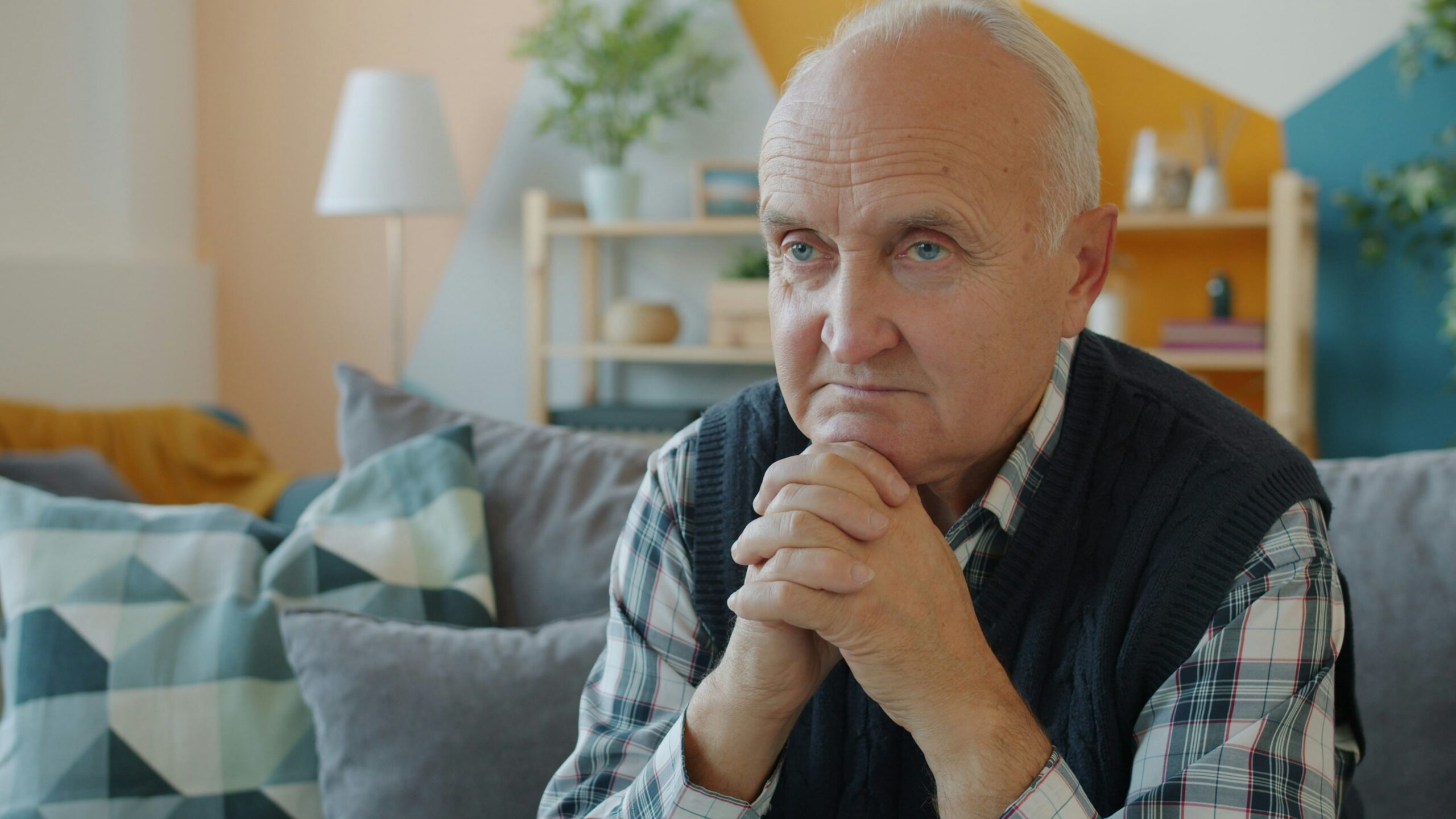 Elderly man sitting on a couch with hands clasped.