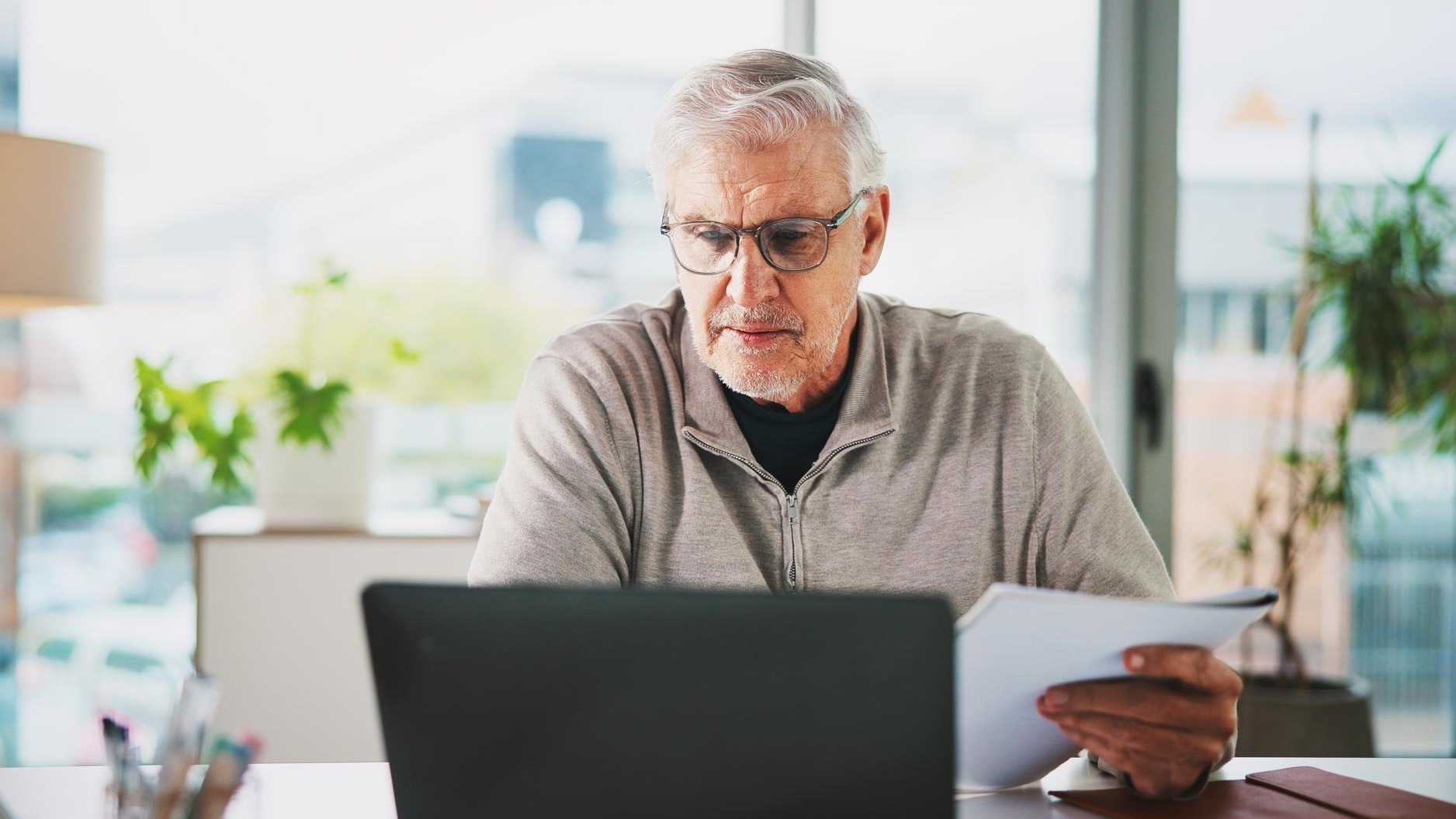 Laptop documents and mature businessman in office with finance report for company budget planning Research paperwork and financial manager with investment proposal for stock market in workplace