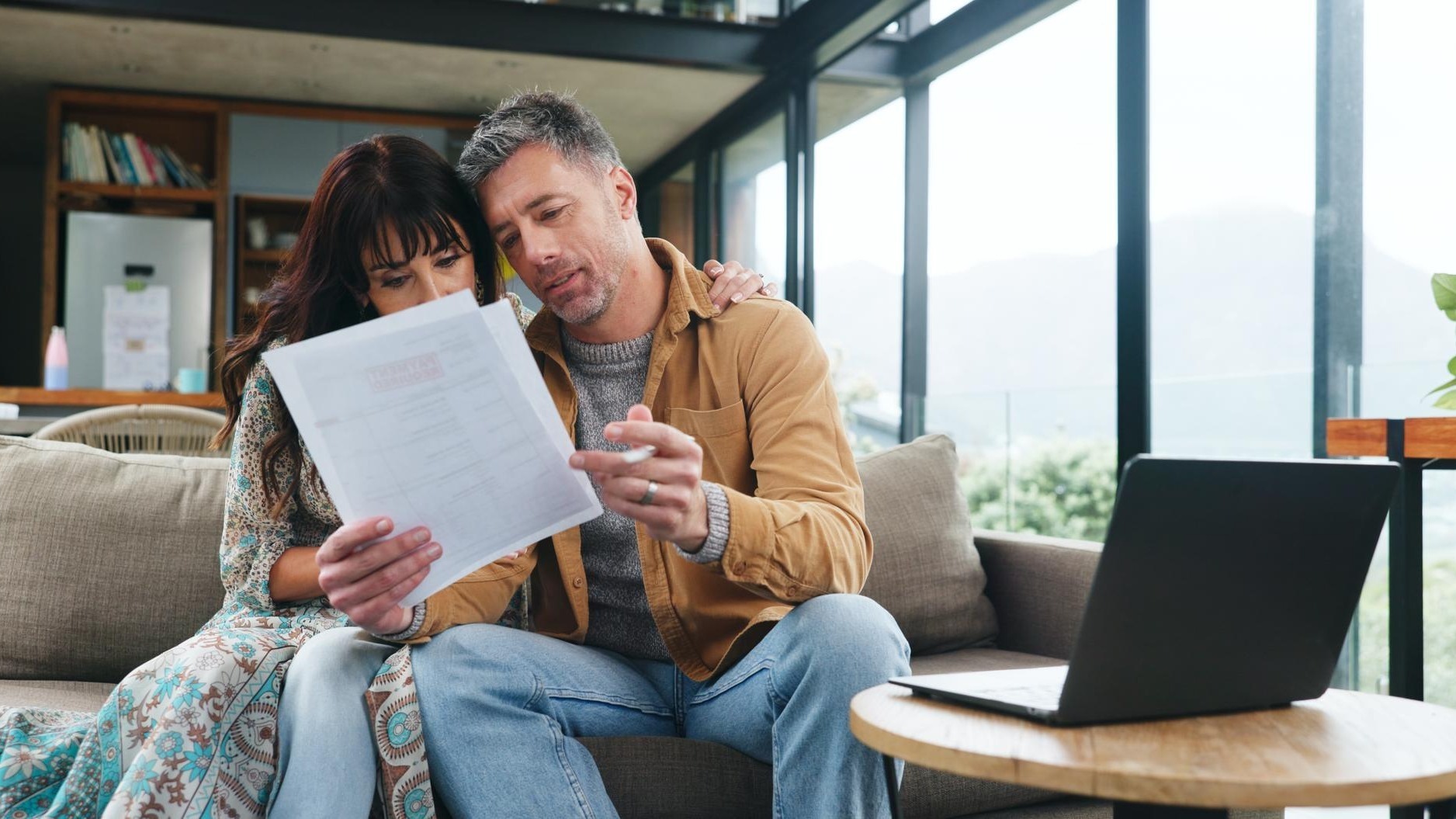 Couple reading and document on couch at house for finance review budget and online payment Mature people laptop and audit paperwork on household expenses financial statement and loan application