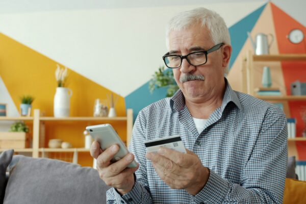 Elderly man using smartphone and credit card for online shopping.