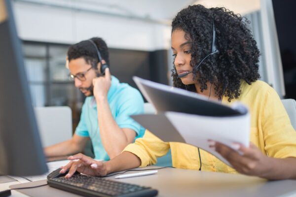Two customer service representatives working with headsets in a modern office setting.