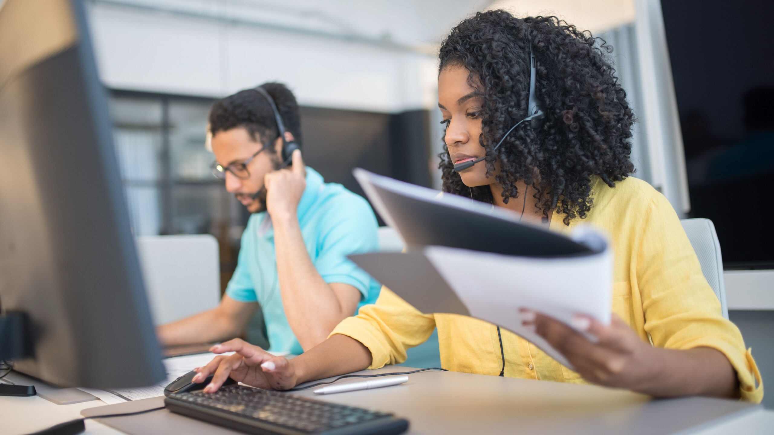 Two customer service representatives working with headsets in a modern office setting.