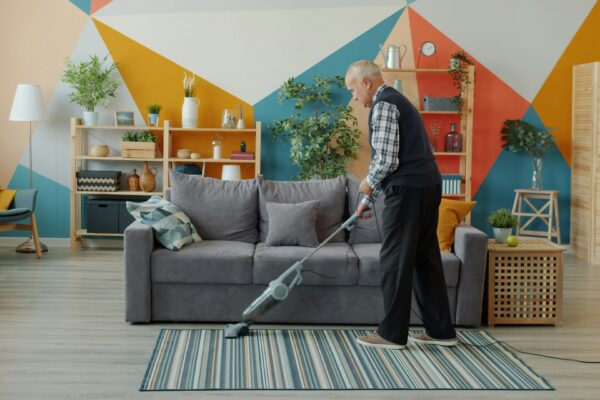 Elderly woman vacuuming a colorful living room floor.