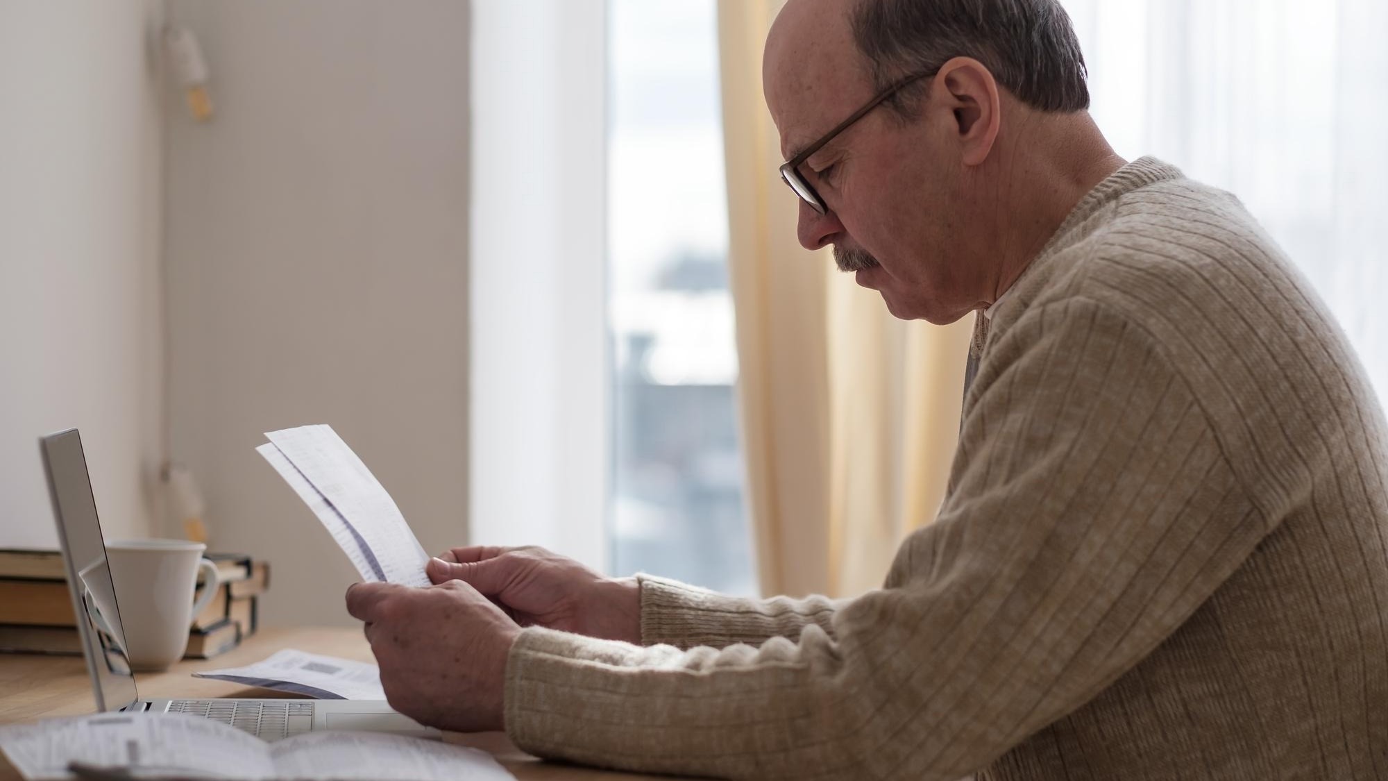 Senior man sitting at table at home alone with paperwork
