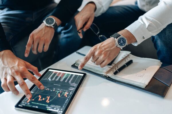 Two businessmen discussing financial data on a tablet during a meeting.