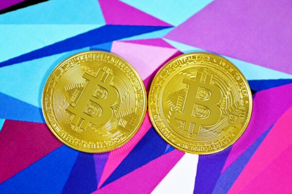 two gold bitcoins sitting side by side on a colorful background