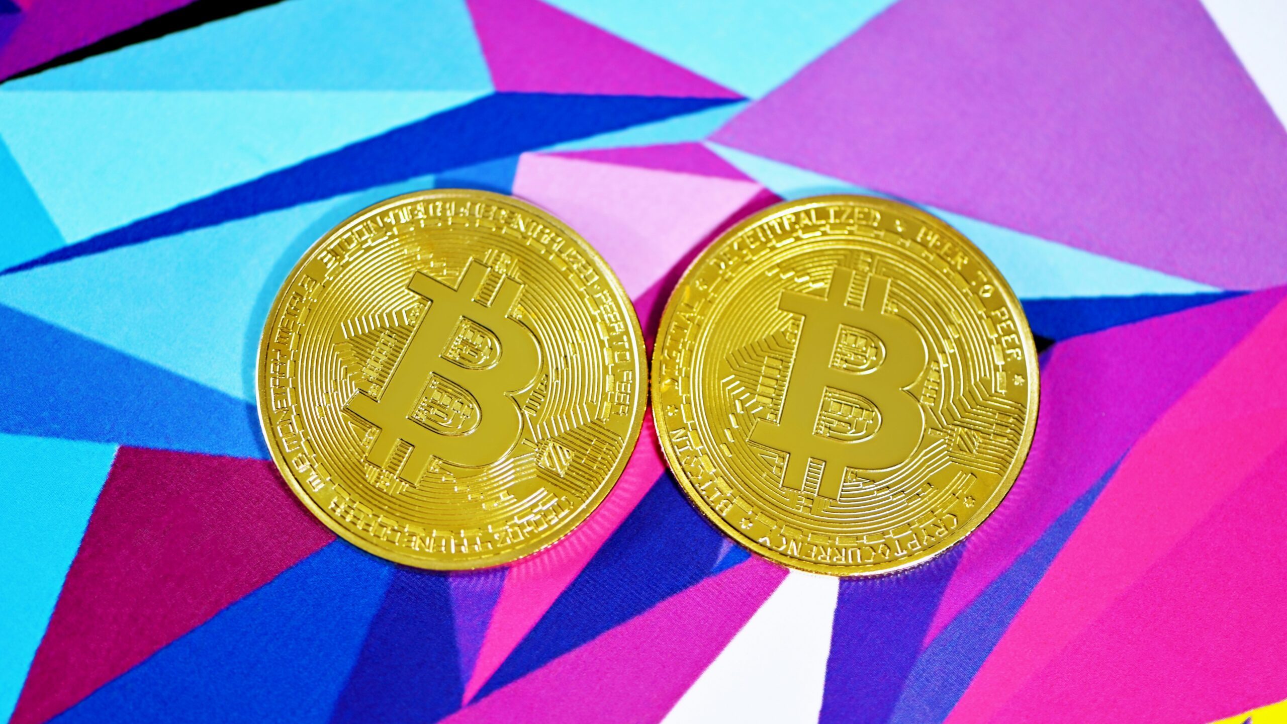 two gold bitcoins sitting side by side on a colorful background