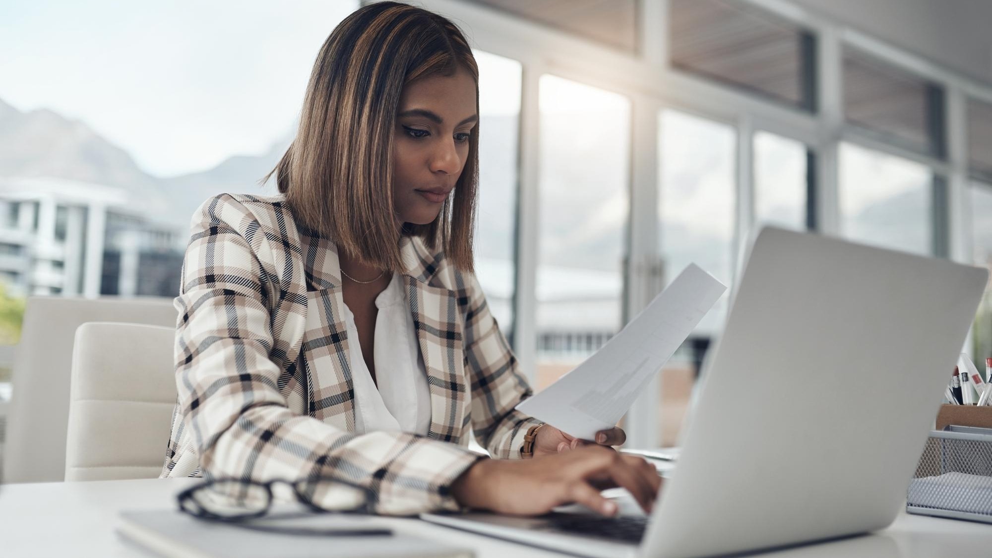 Business analyst laptop and woman typing documents in office workplace Paperwork analysis computer and female Indian person reading analytics for data graphs or charts for finance statistics
