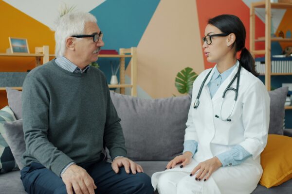 Doctor talks with an elderly patient on a couch.