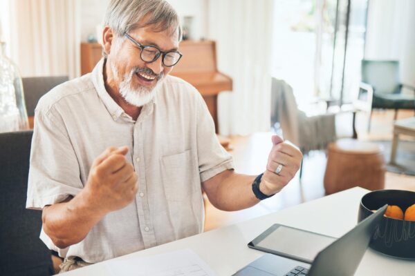 Senior man winner and laptop for home success celebration and stock market or financial investment Asian trader or entrepreneur with yes fist and excited for bonus news or trading on computer