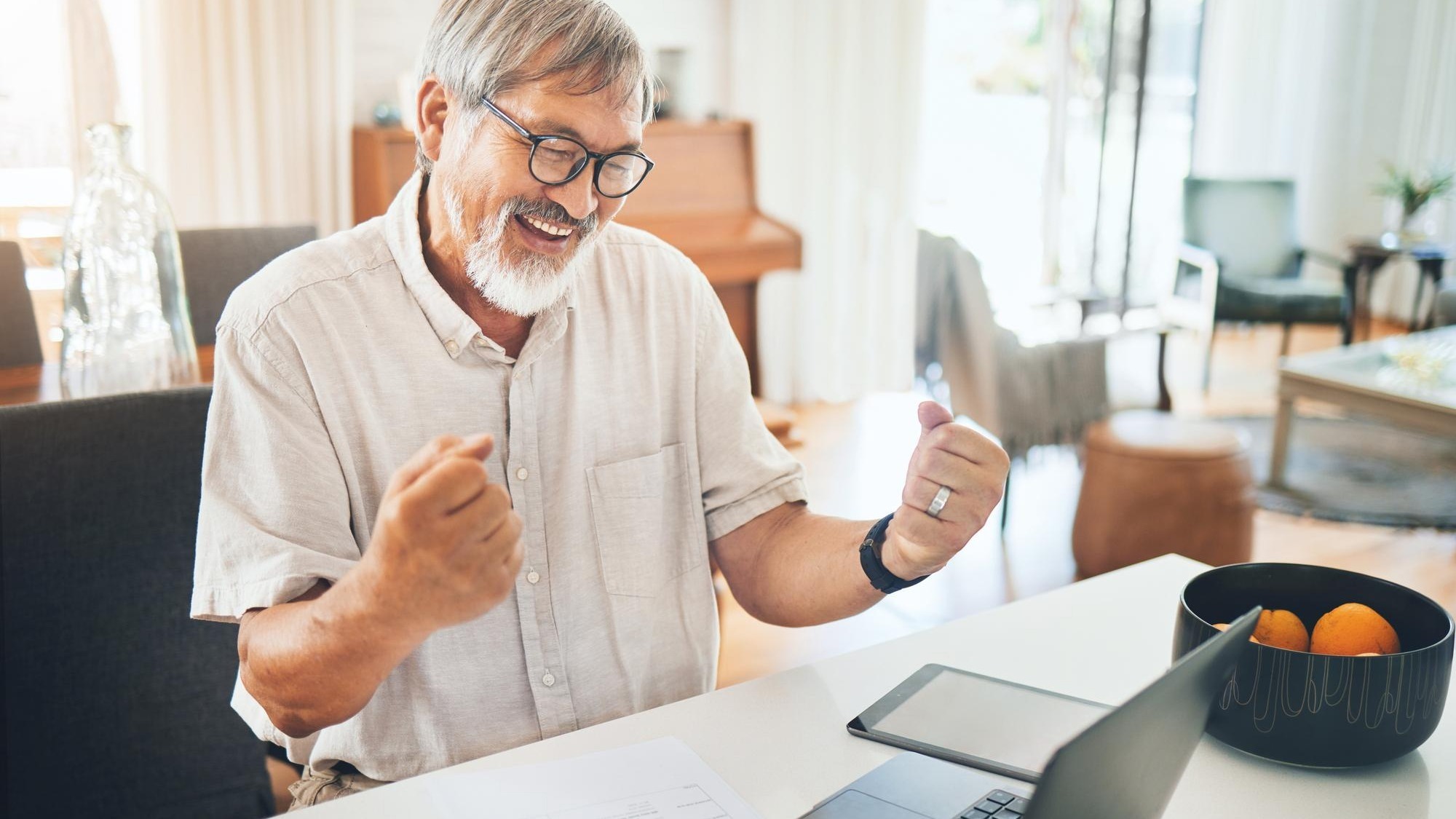 Senior man winner and laptop for home success celebration and stock market or financial investment Asian trader or entrepreneur with yes fist and excited for bonus news or trading on computer