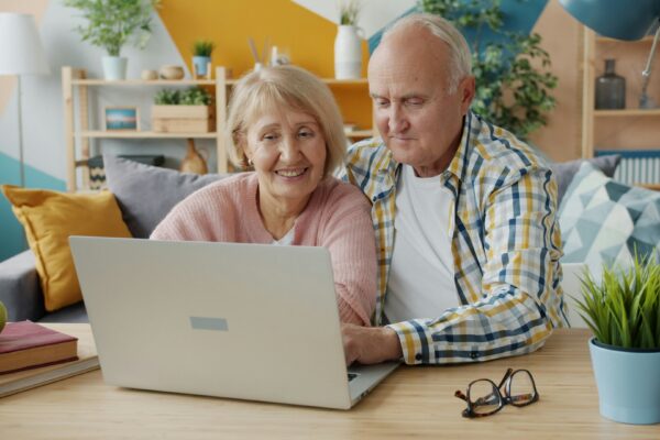Elderly couple smiling while looking at laptop together.