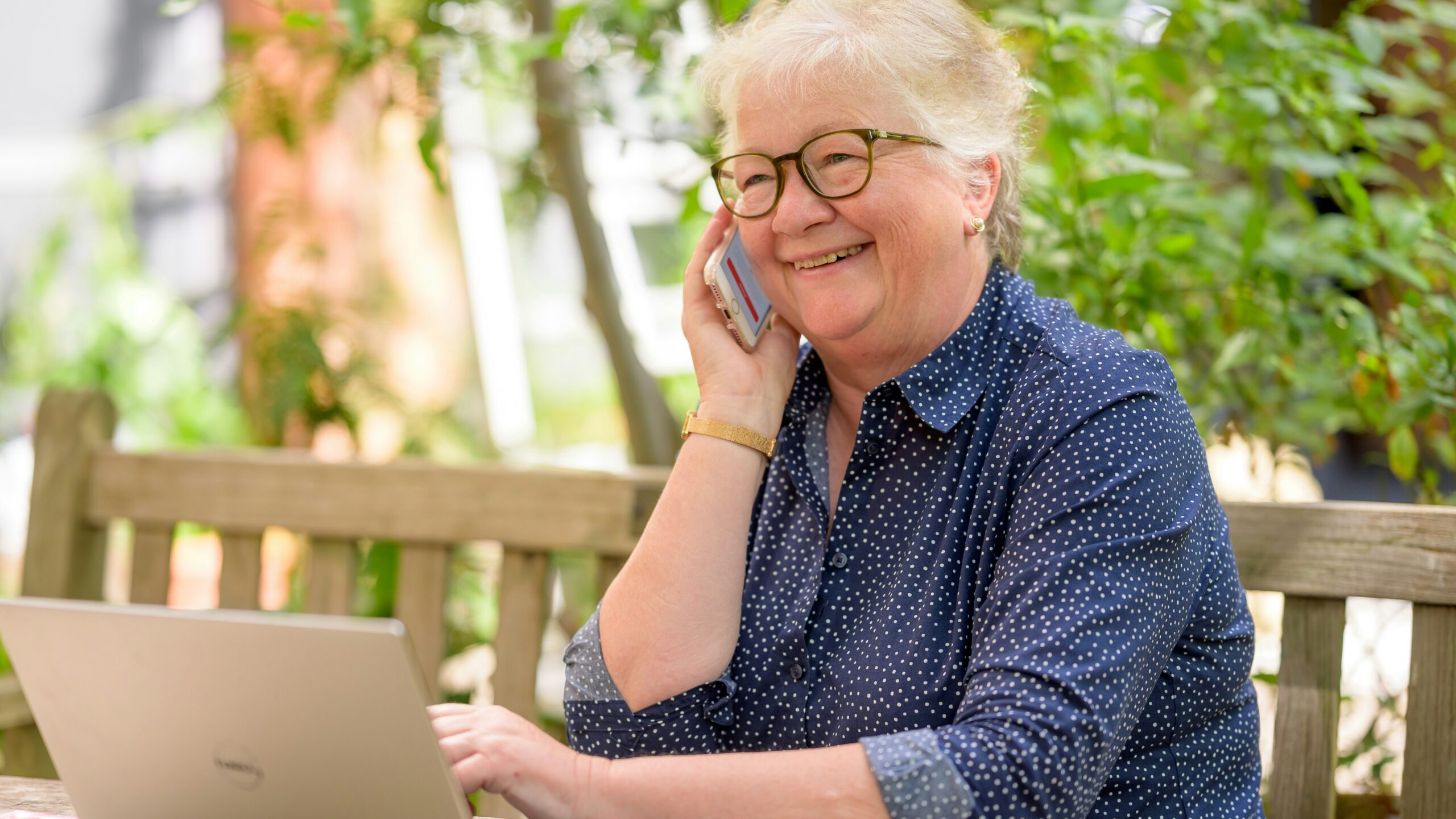 a woman on her phone while sitting at a table with a laptop