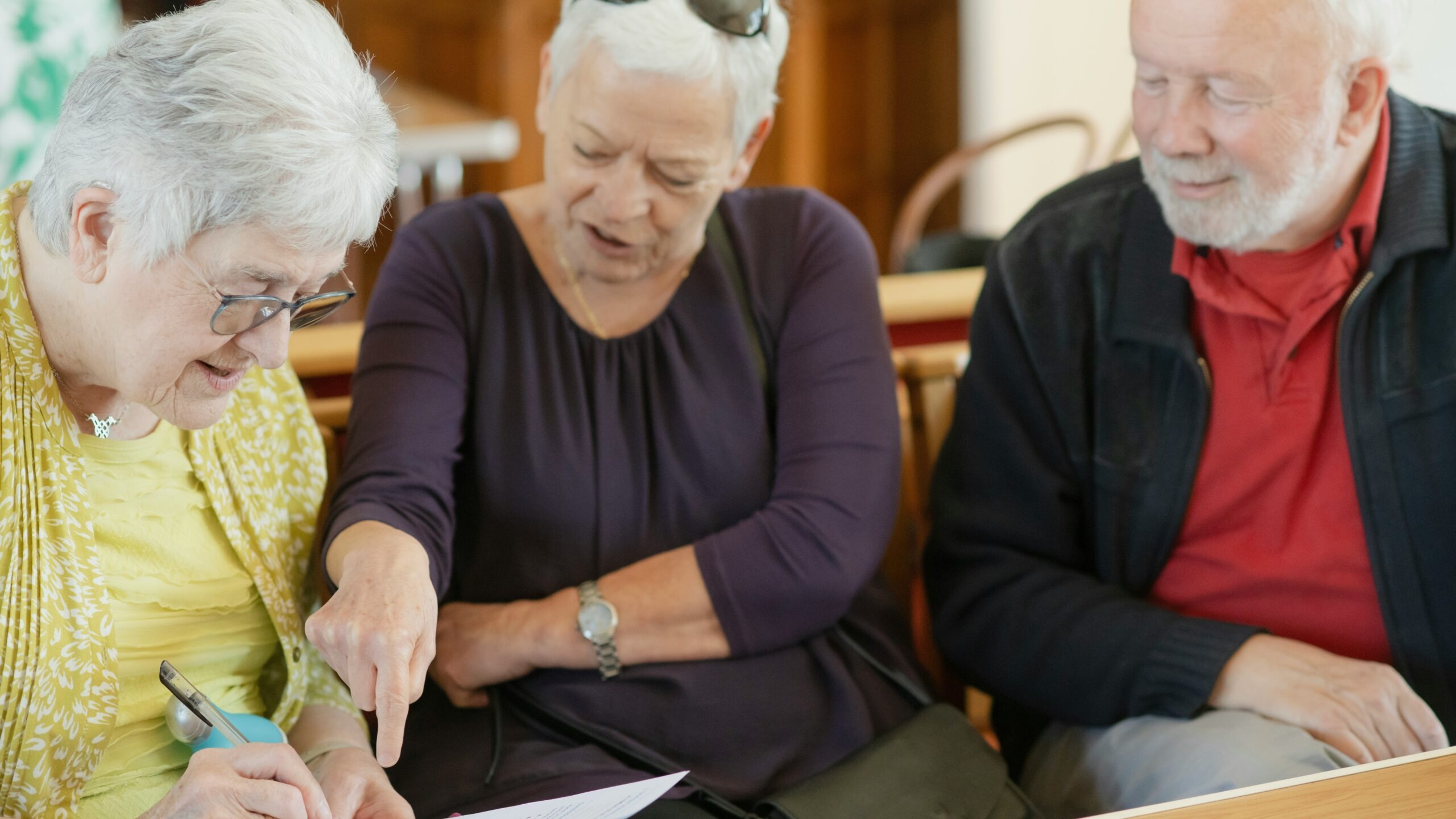 Three older adults are looking at a paper.