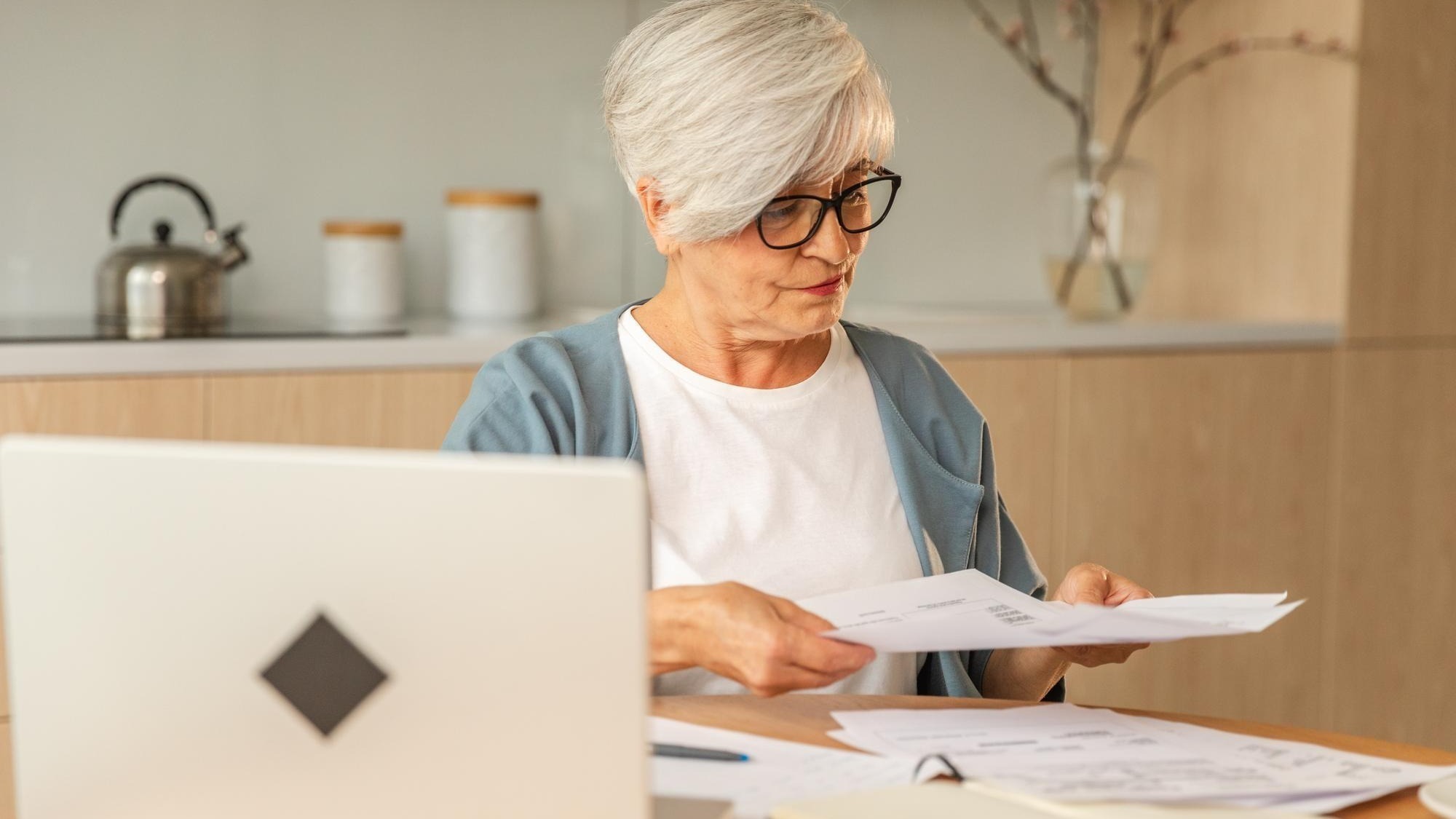 Middle aged senior woman sit with laptop and paper document pensive older mature lady reading paper