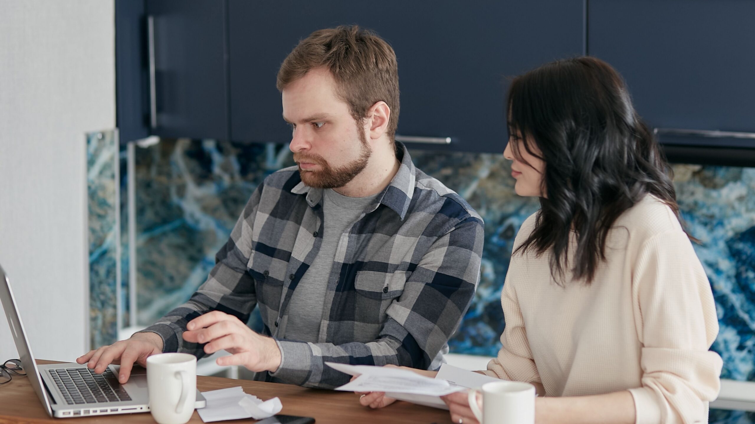 A couple working together on a laptop managing finances at home, showcasing teamwork and concentration.