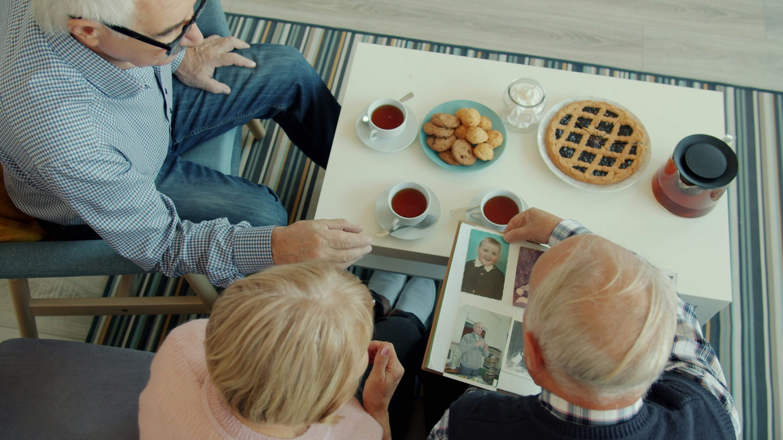 Seniors looking at a photo album with tea and snacks
