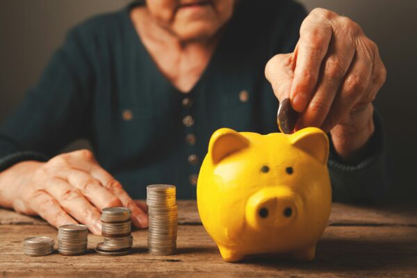 Elderly hands depositing coins into a yellow piggy bank