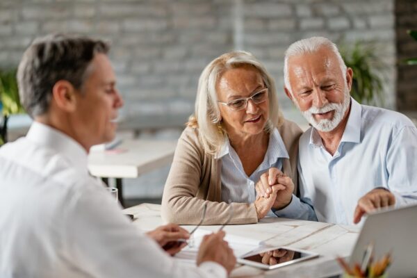 Happy senior couple holding hands and using laptop while having a meeting with financial advisor in the office Senior man is pointing at something on laptop