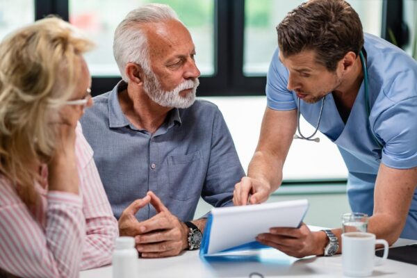 Serious doctor discussing with senior couple about their medical documents during appointment at clinic