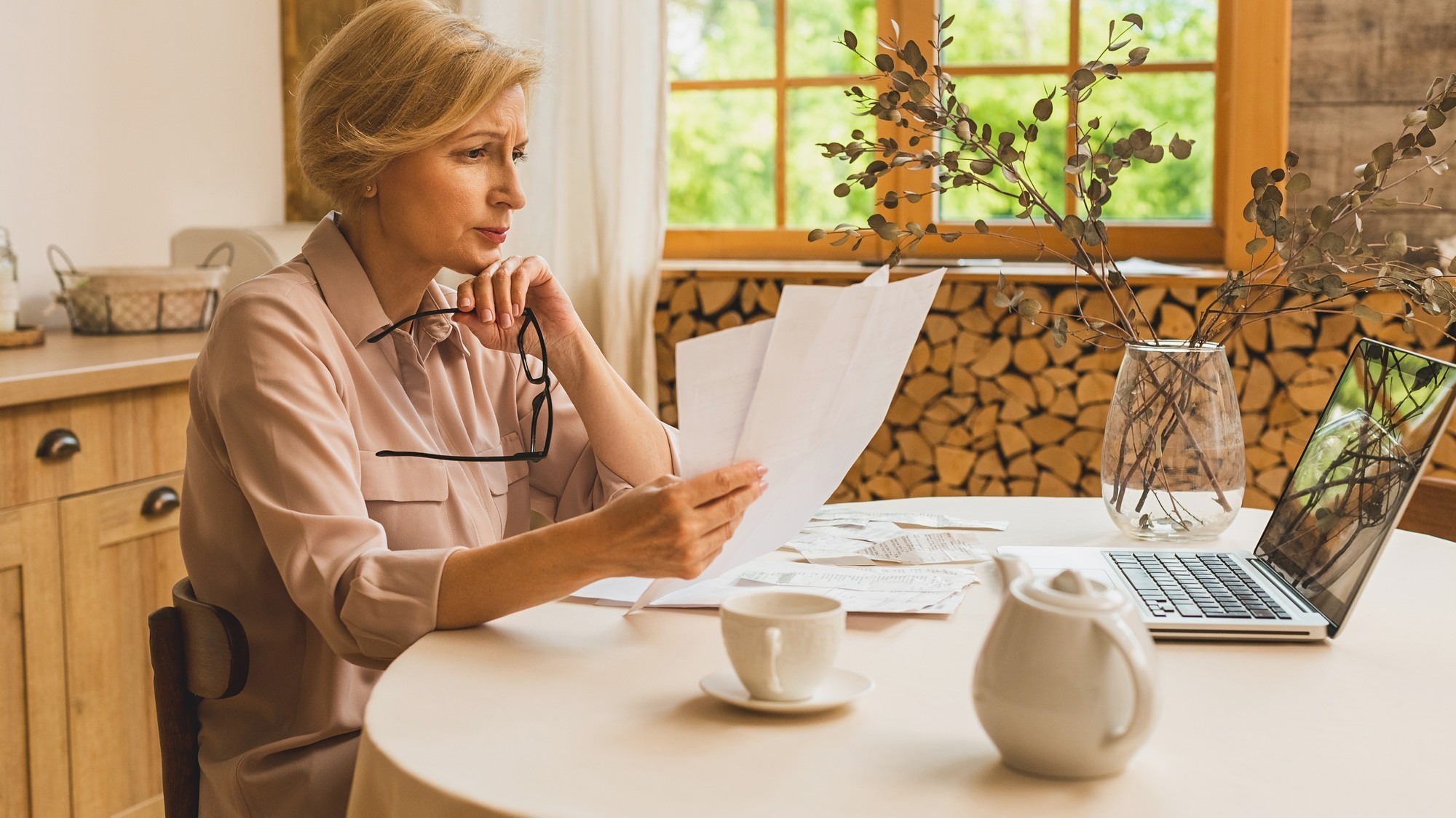Middle aged mature senior woman holding paper bill or letter using laptop computer at home for making online payments on website, calculating financial taxes fee cost, reviewing bank account.