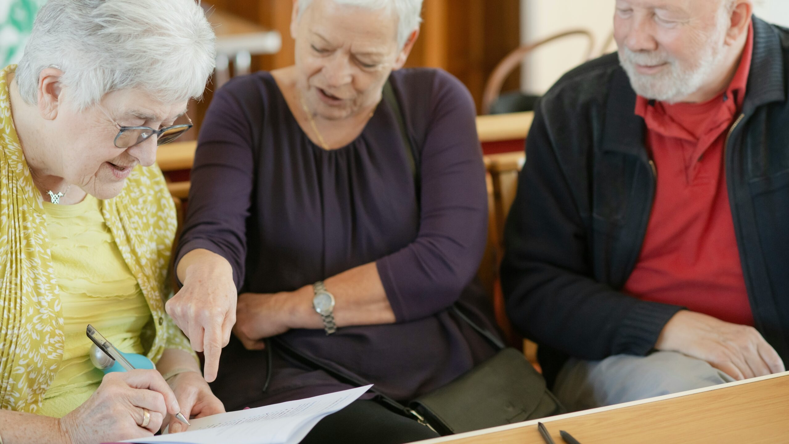 Three older adults are looking at a paper.