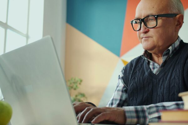 Elderly man with glasses working on a laptop.