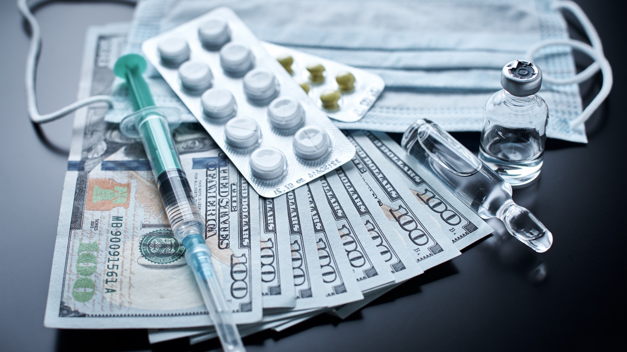 Pills, protective mask, medical items and dollar bills on dark background. Expensive medicine concept. Pharmaceutical industry and medical insurance