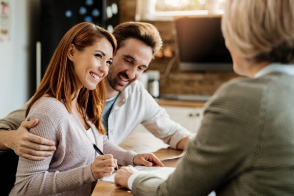 Young happy woman and her husband signing an agreement with insurance agent during a meeting