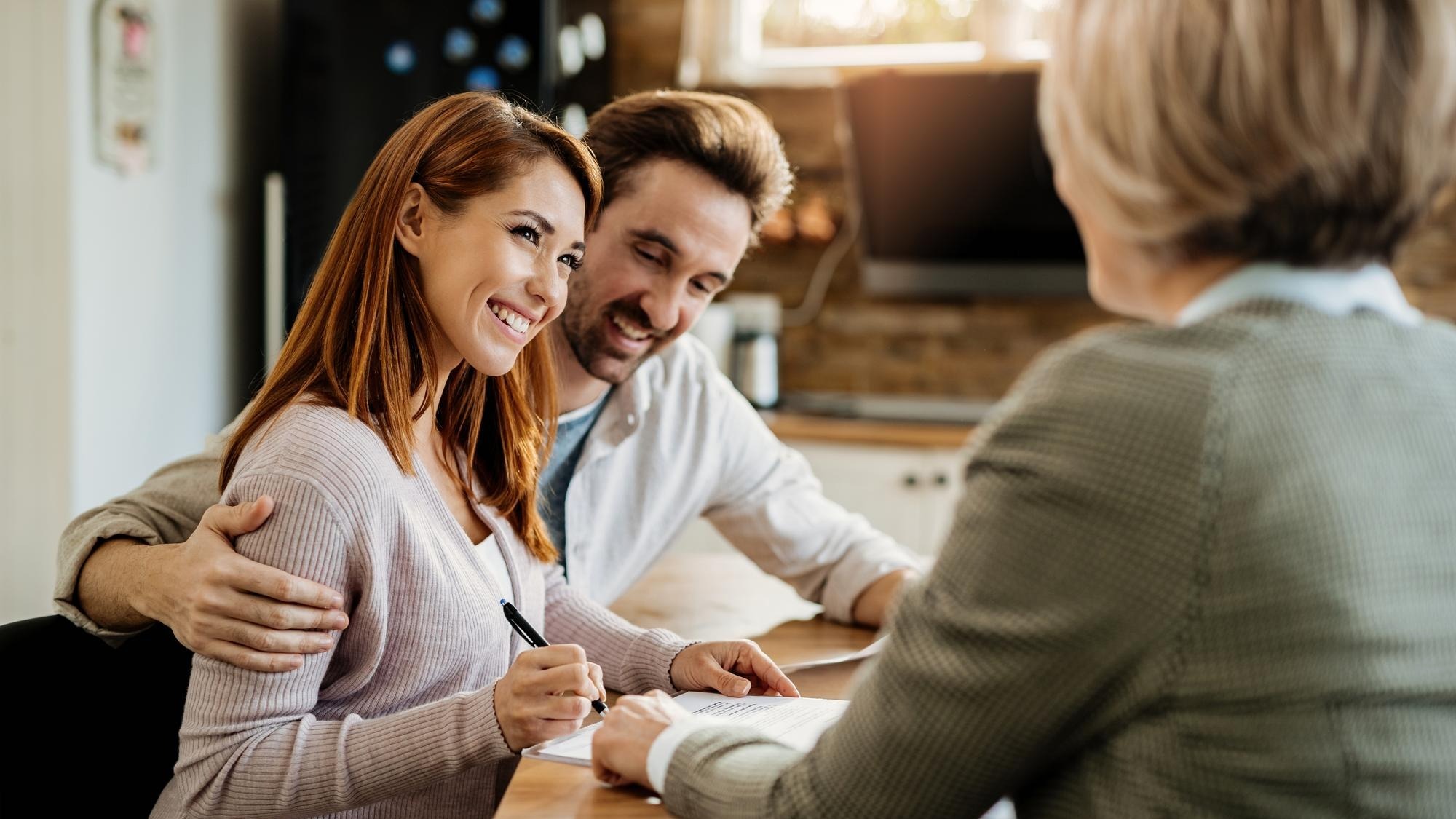 Young happy woman and her husband signing an agreement with insurance agent during a meeting